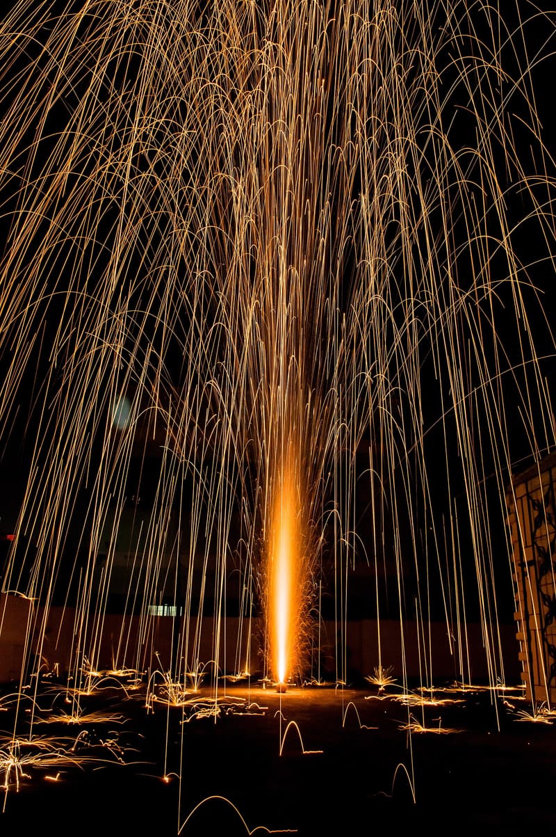 A flower pot cracker throwing a tall fountain of golden sparks at night