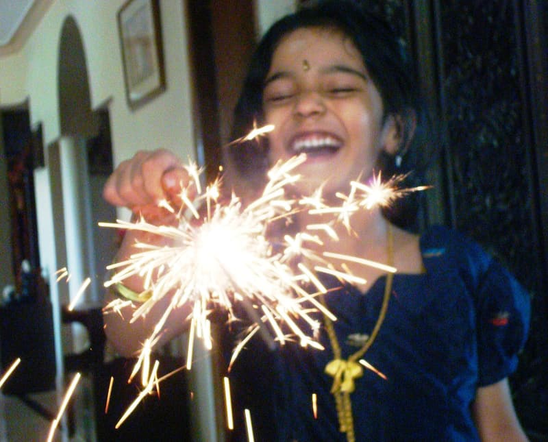 A smiling girl holding a lit sparkler on Deepavali